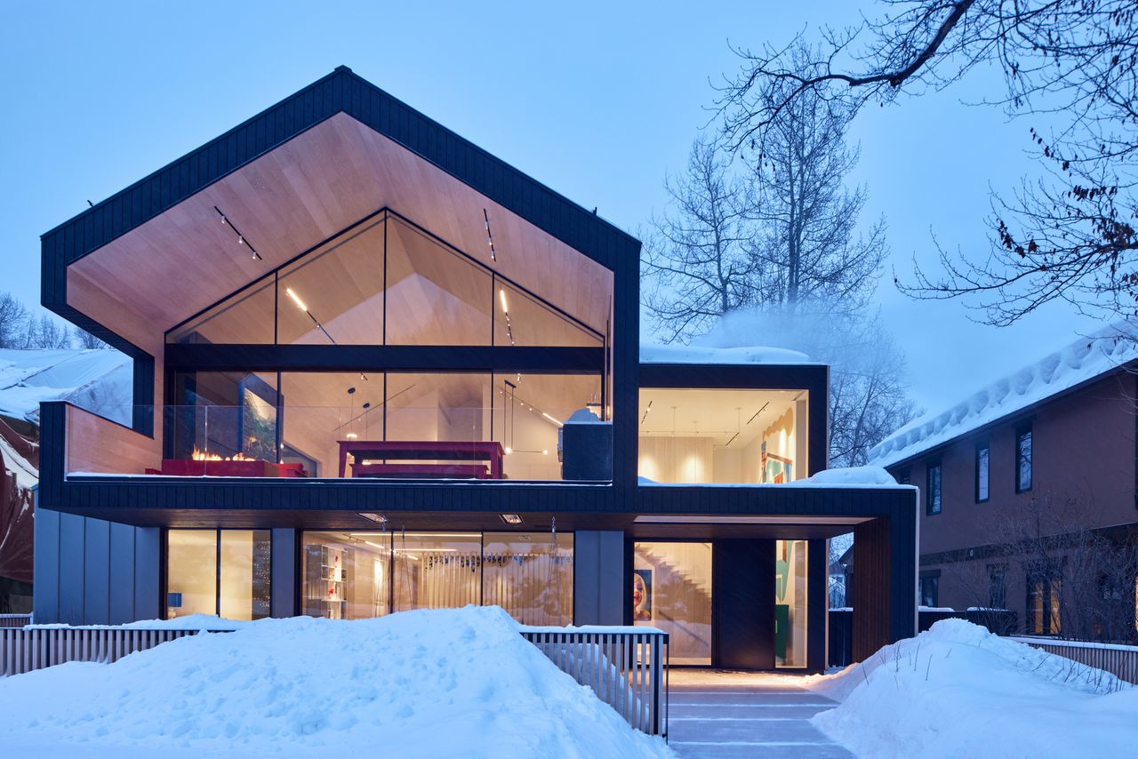 A clean-lined exterior of an Aspen home with large windows and a yard covered in snow.