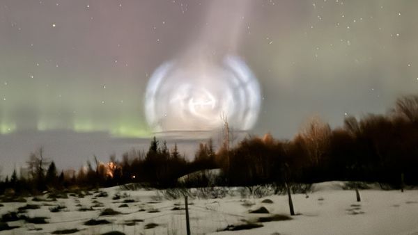 A massive spiral of white light in the night sky with auroras in the background