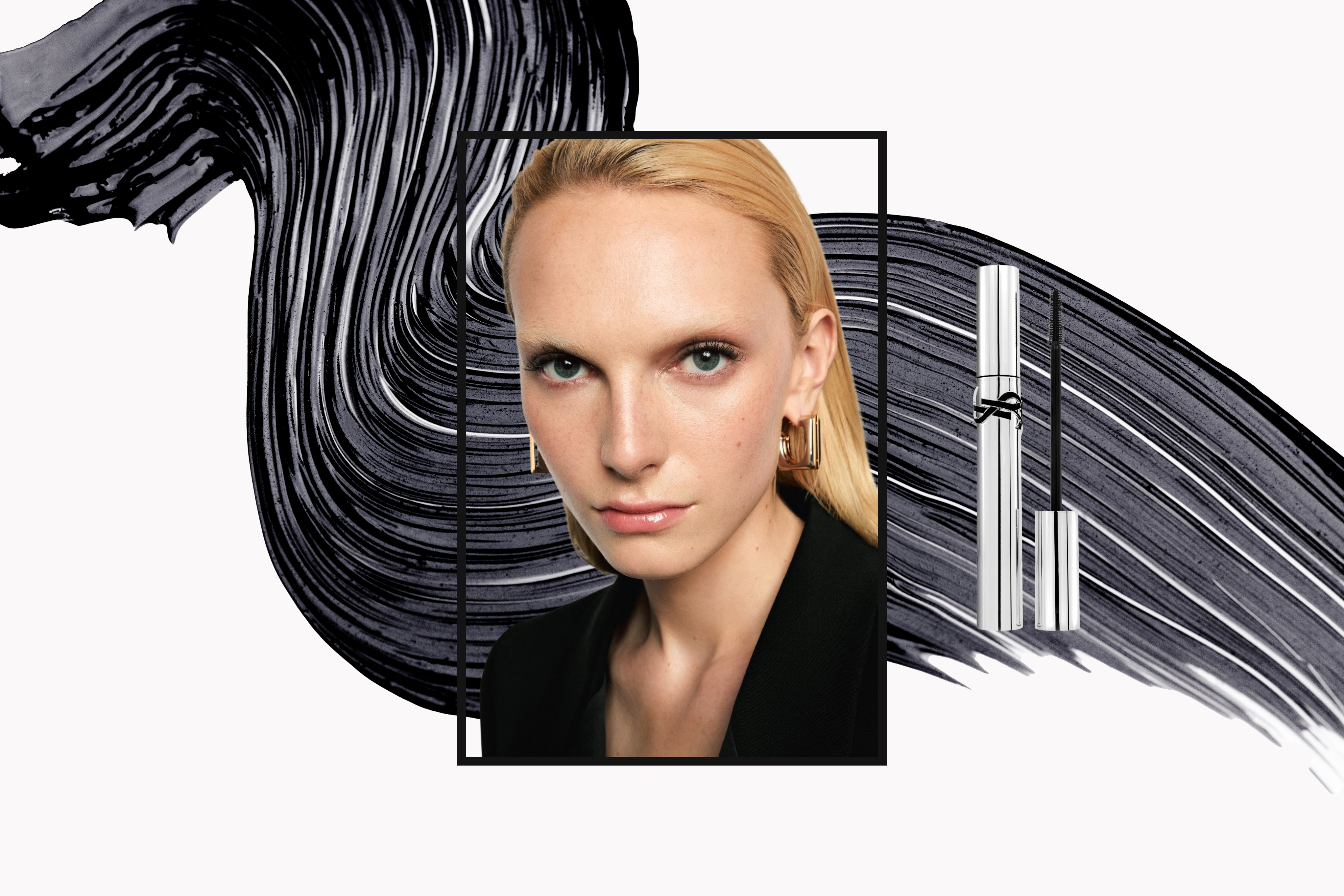A picture of a blonde woman with fair skin enclosed in a black border. She is in front of an abstract mascara swatch. Beside her is a silver tube of YSL mascara. 