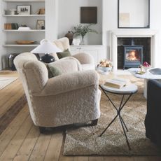 living room wood floor ideas, living room with tactile sheepskin style armchairs, rattan rug, natural floor boards, side tables, log burner, bookcases