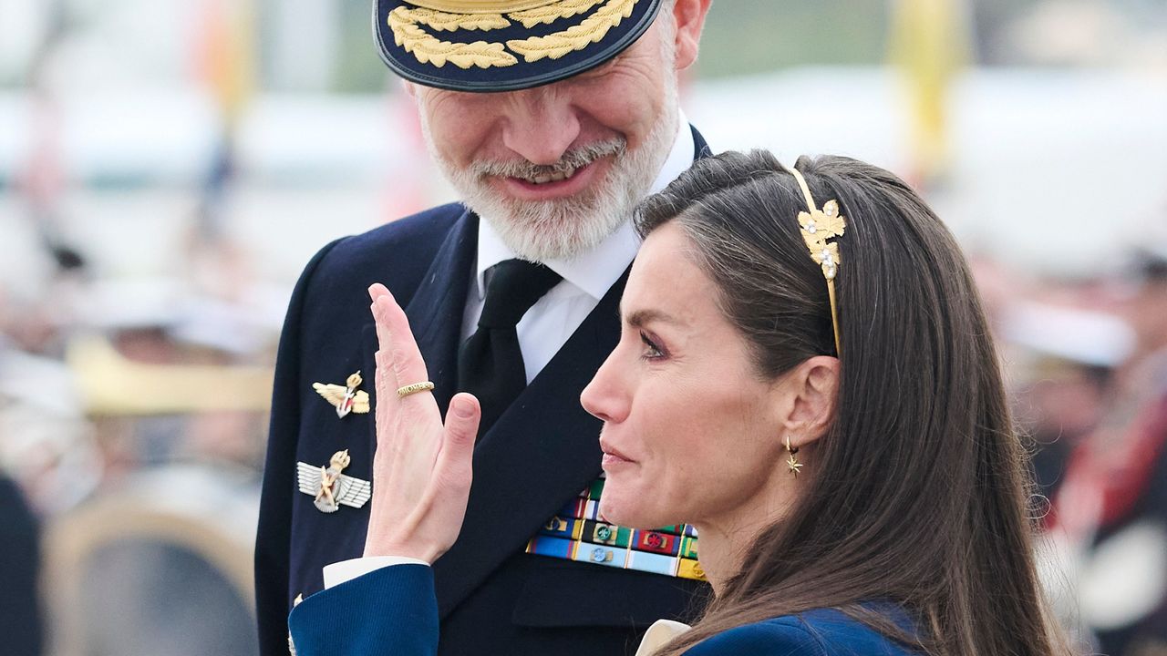 Queen Letizia wearing a blue suit and covering her face with her hand as King Felipe looks down on her 