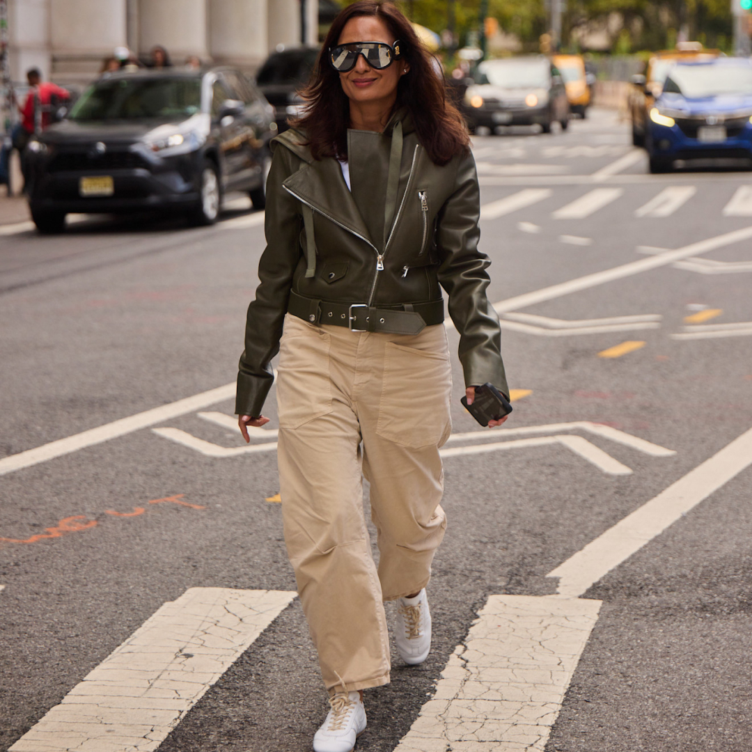 Fashion week attendee wearing leather jacket, beige pants, white sneakers, and sunglasses