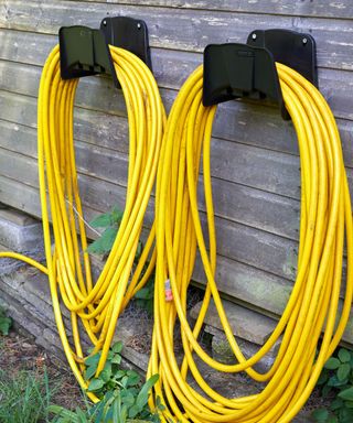 yellow Hose pipes neatly coiled on a pair of storage hangers attached to wall
