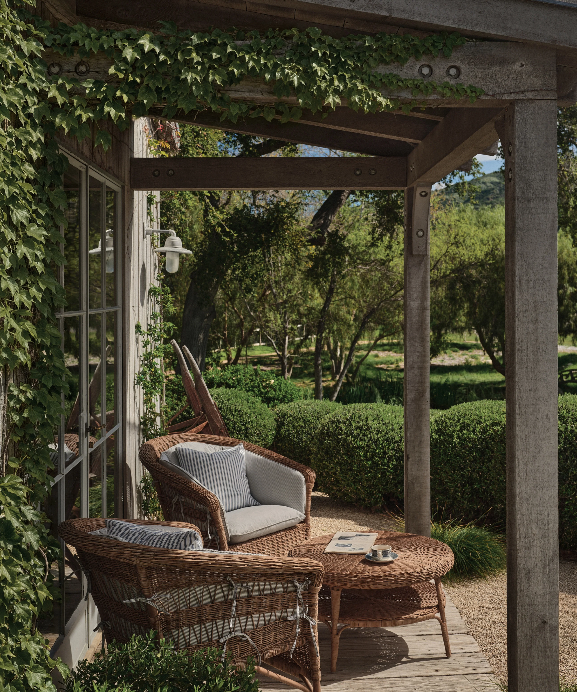 a deck with two wicker deck chairs, a round wicker coffee table, and ivy growing on the porch overhang