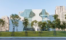 National Taichung Theater - A freeform white building with white walls and curved floor to roof windows, set in a garden with trees