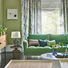 Green living room with green sofa, wicker side table, and floral curtains