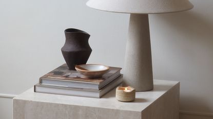 a side table with a candle, books, incense bowl, lamp and vase on top