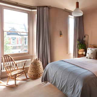 a bedroom with a bay window dressed with curtains and a rocking chair in front