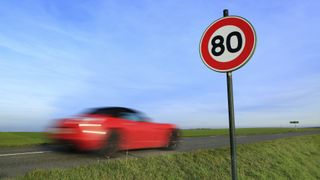 A photo of a red car driving past a speed limit sign