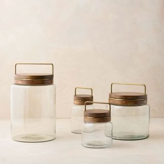 Four glass canisters with brown wooden lids and brass metal handles