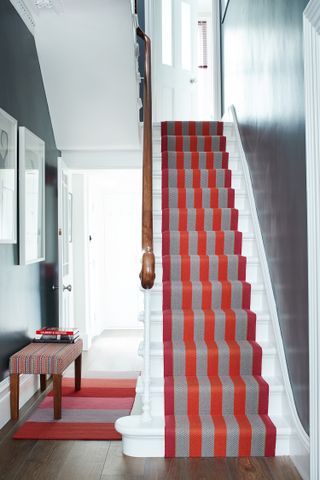 A dark grey hallway with striped red and grey staircase carpet runner up by Roger Oates