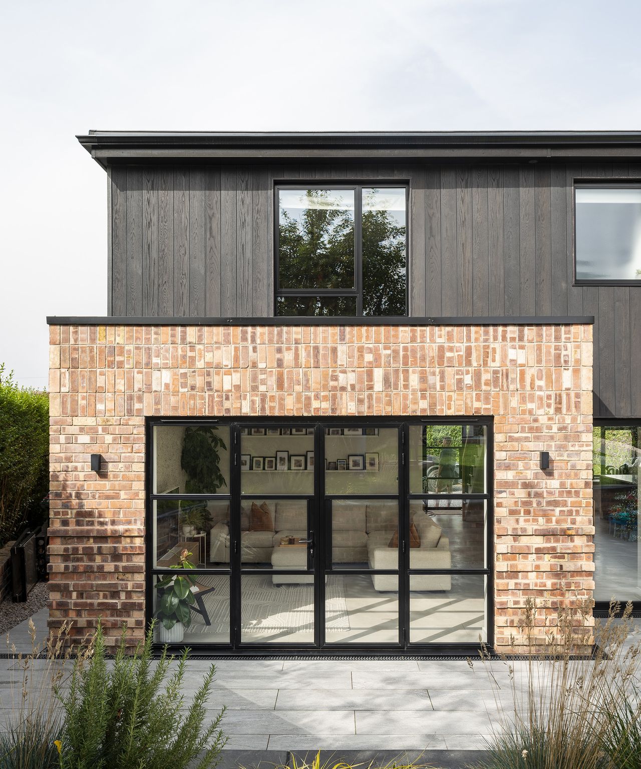 A brick extension with large glass Crittal-style doors opening out to a paved patio area