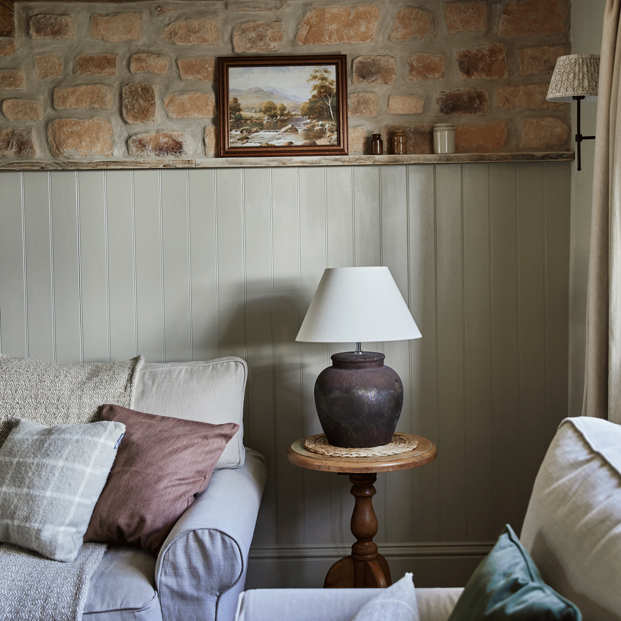 a living room with exposed stone wall and wood cladding a sofa and armchair a side table with large lamp