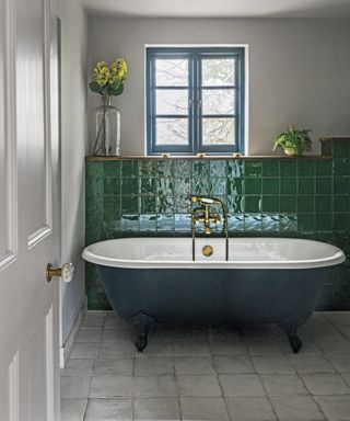 An ensuite with green wall tiles and a dark green free-standing bath