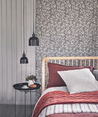 Double bed with a wooden bedhead in front of floral tapestry wall hanging. Hanging fabric on the wall. Pendant lights