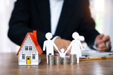 A model house beside stacks of coins sitting on a table.
