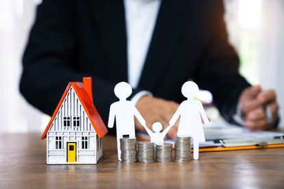 A model house beside stacks of coins sitting on a table.