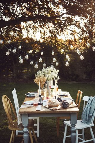String garden lights above an outdoor dining table with wooden chairs