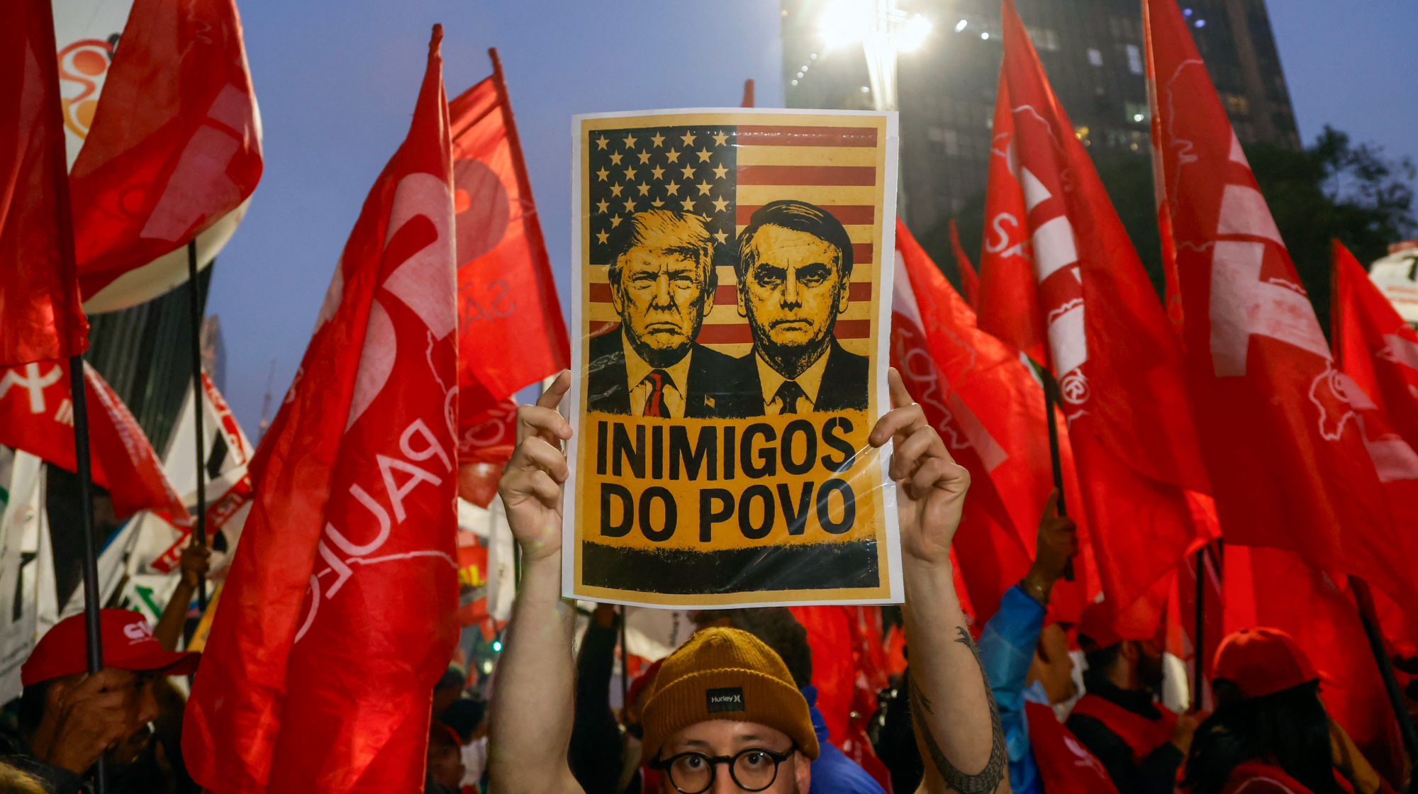 A man holds a sign with images of US President Donald Trump and former Brazilian President Jair Bolsonaro that reads "Enemies of the people" during a demonstration calling to tax the super-rich and demanding the end of the six-day workweek in Sao Paulo, Brazil, on July 10, 2025