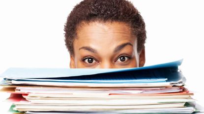 A woman peeks out above a pile of paperwork.