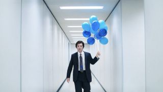 Adam Scott's Mark Scout is shown walking down a white hallway holding a bunch of blue balloons in an Apple TV+ image from Severance Season 2.