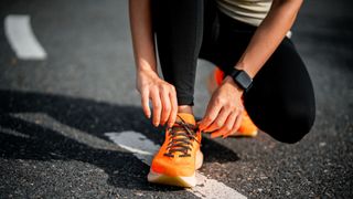 Woman tying up orange running shoes during a race