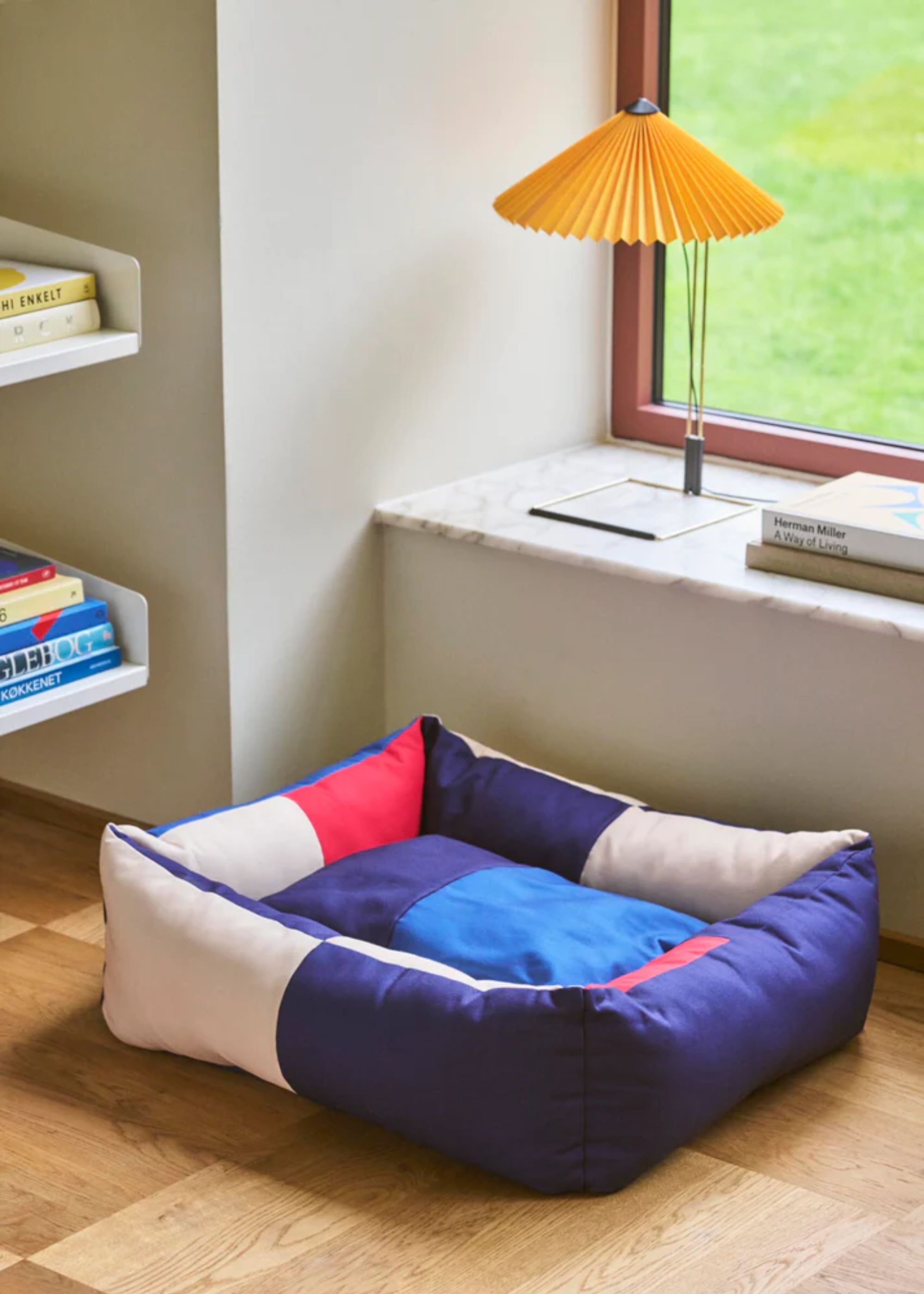 A multicolor pet bed from HAY by a window