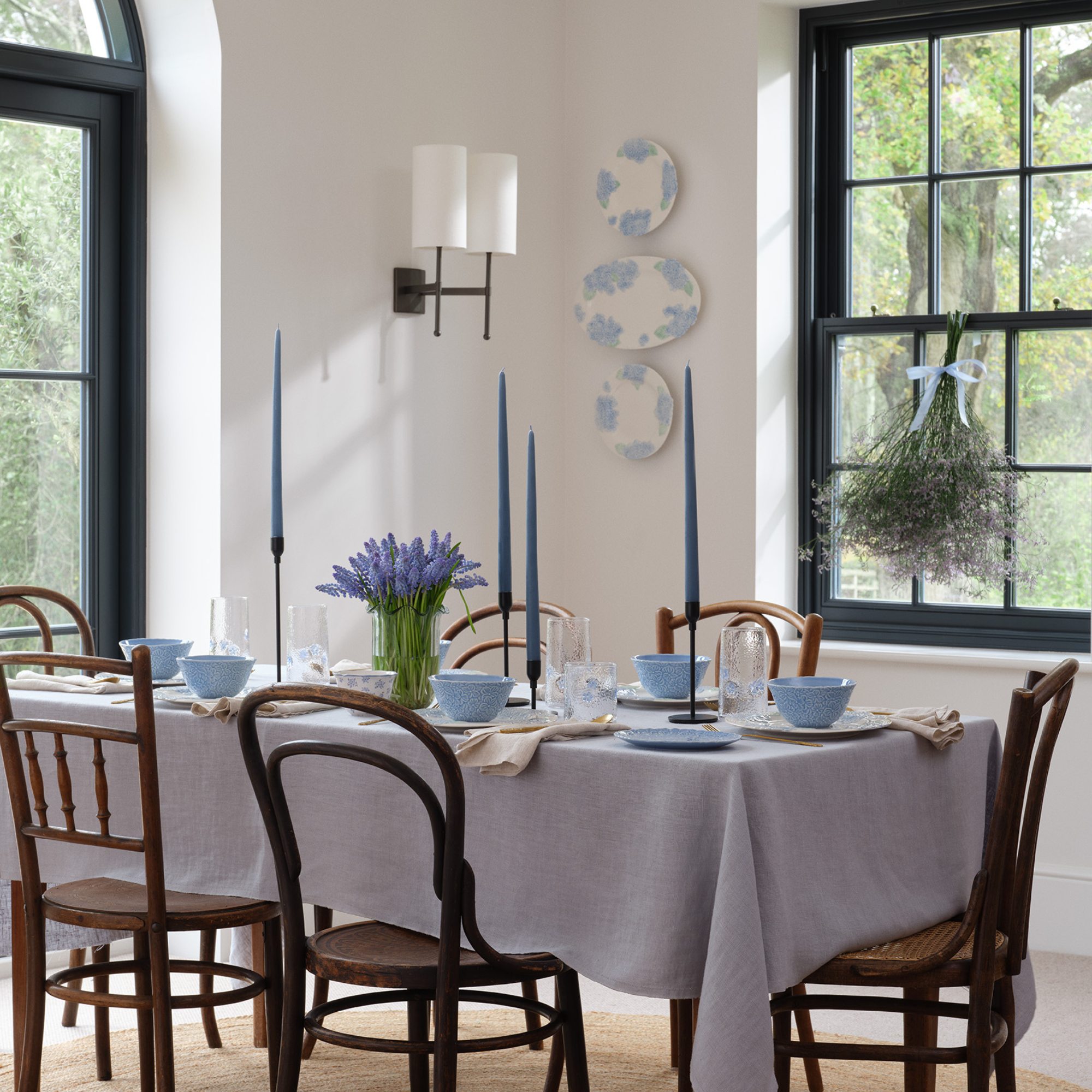 Dining room table, with soft blue crockery, lavender table cloth, tall blue candles and a vase of purple flowers.