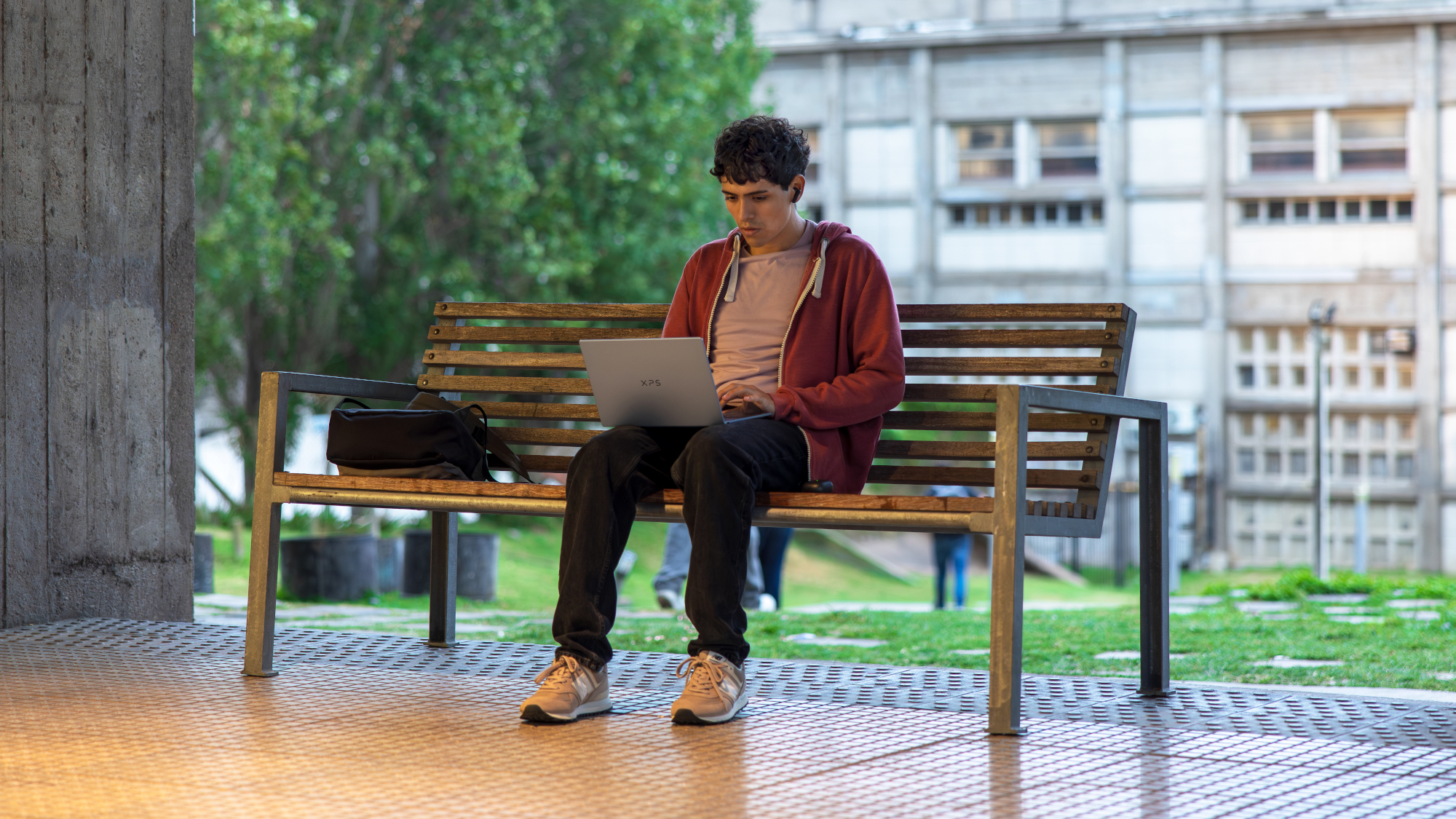 Dell XPS 13 being used by a young person sat on a bench, you can see the laptop lid and XPS logo
