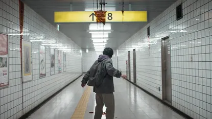 A man stands in a creepy subway station underneath a sign for "Exit 8". The sign is covered in blood.