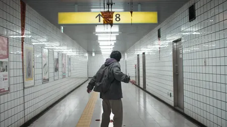 A man stands in a creepy subway station underneath a sign for "Exit 8". The sign is covered in blood.