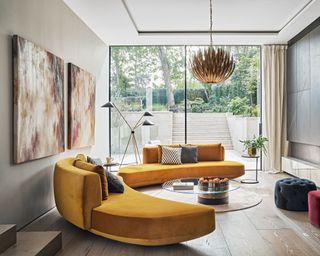 Living room ceiling light ideas with curved modern yellow sofas and a statement gold pendant