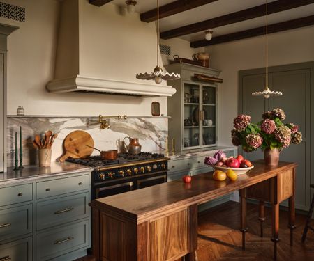 A traditional kitchen with mid-blue cabinets, white walls, a marble countersplash, a wooden island, and vintage vessels on the counters