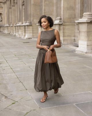 Woman on street wears dark grey dress, flip flops and brown handbag