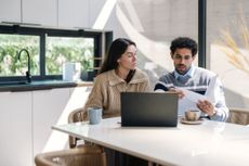 Couple look at finances as they sit at kitchen dining table.