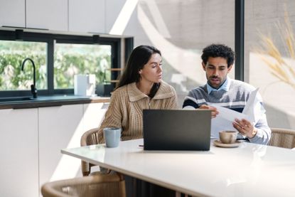 Couple look at finances as they sit at kitchen dining table.