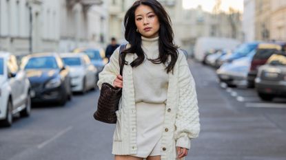 TingTing Lai wears creme white cardigan, shorts, turtleneck, brown bag, knee high boots during the Berlin Fashion Week AW23 on January 19, 2023 in Berlin, Germany. 