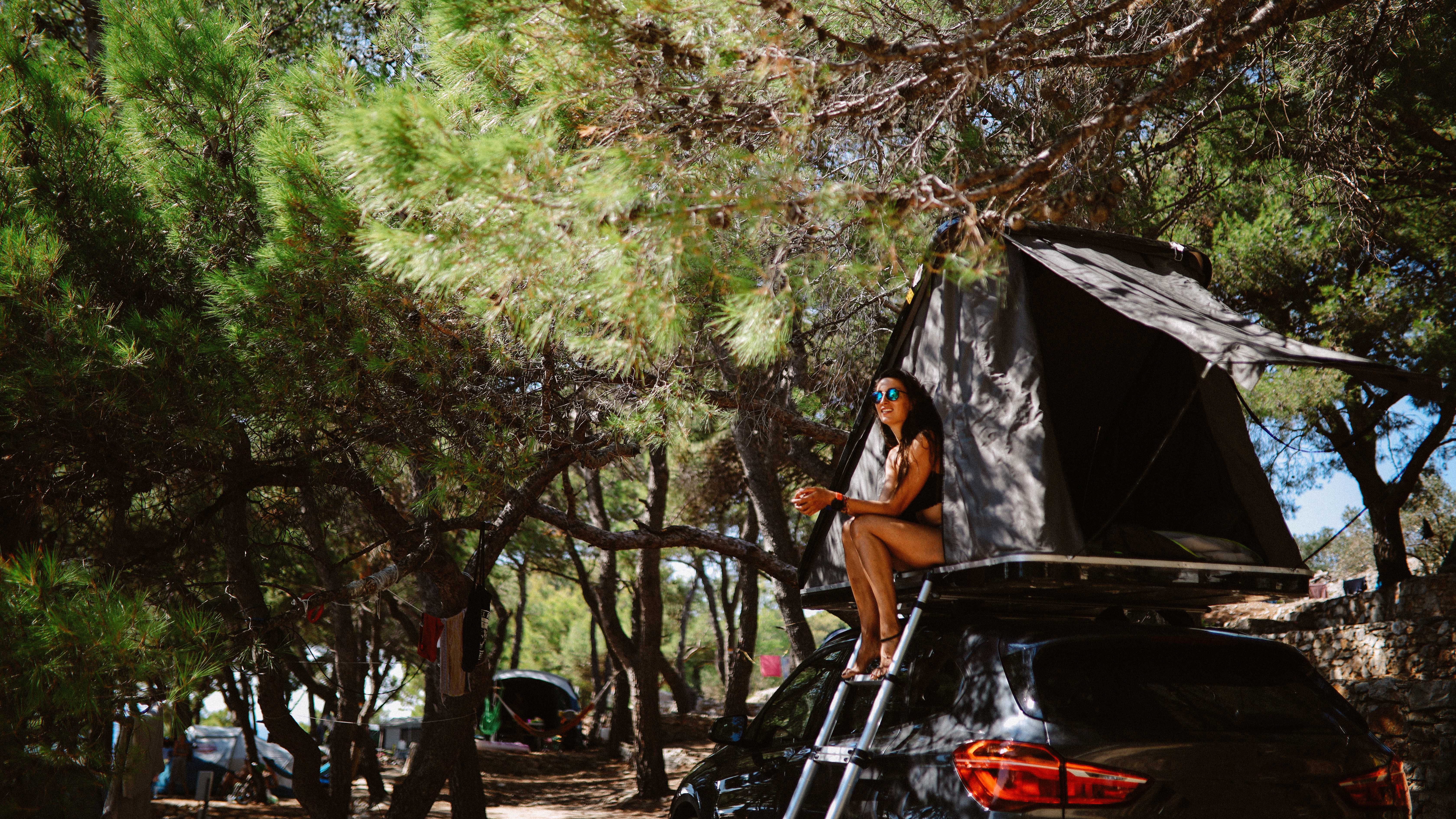 Woman sits in the door of a rooftop tent in a campsite