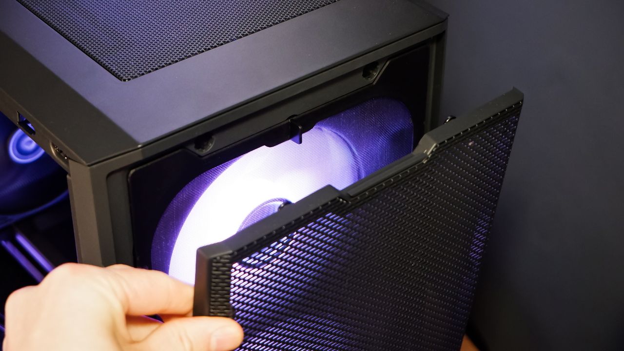 A gaming PC sat on a desk with purple RGB lighting on the fans and light bar enabled.