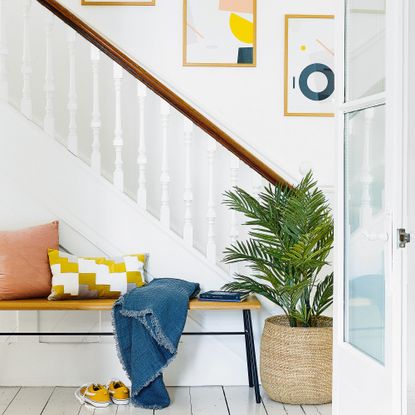 White stairwell with wooden bannister, yellow picture on the wall and bench next to stairs