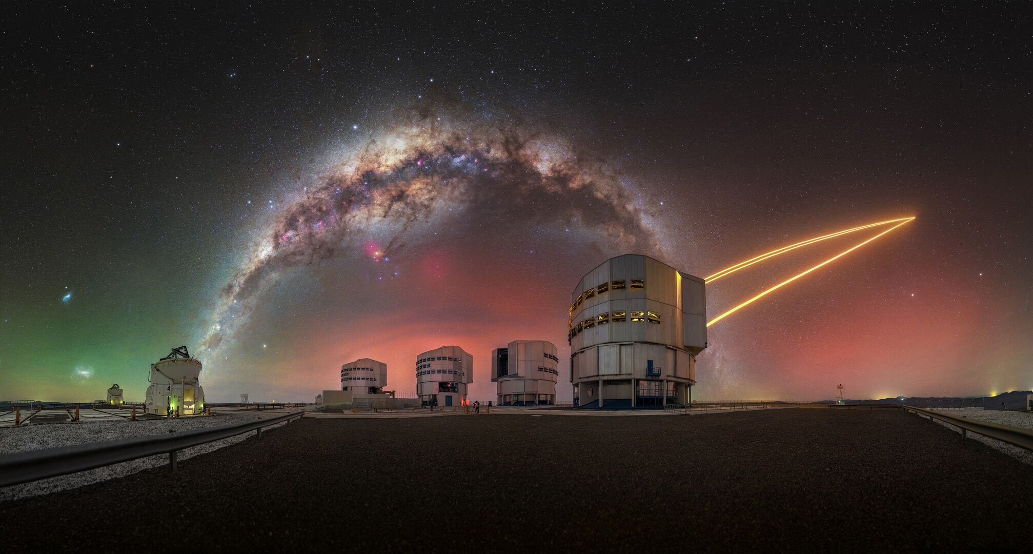 A night sky image shows the glowing Milky Way galaxy above four buildings, with a series of bright yellow lines moving toward the top right of the image