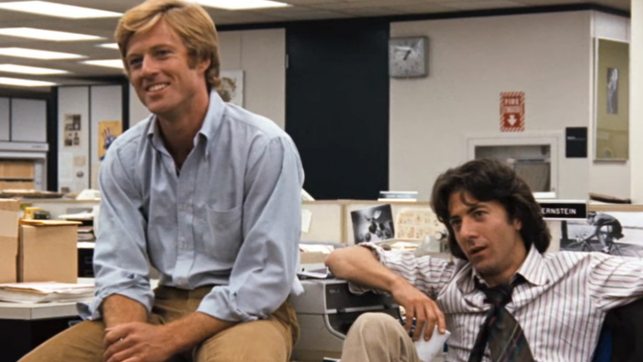 Robert Redford smiling, sitting next to Dustin Hoffman in All the President's Men