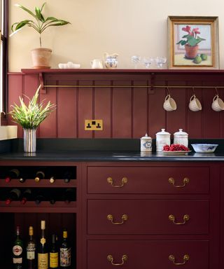 kitchen countertop trends, dark red kitchen cabinets with black granite countertop, open shelf, brass hanging rail, brass handles on drawers, wine bottle storage, artwork