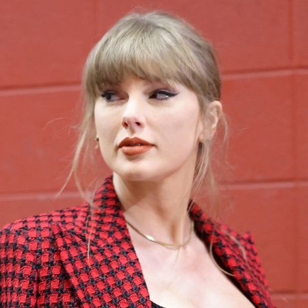 Taylor Swift wears a red and black houndstooth jacket, a black corset, and red lipstick