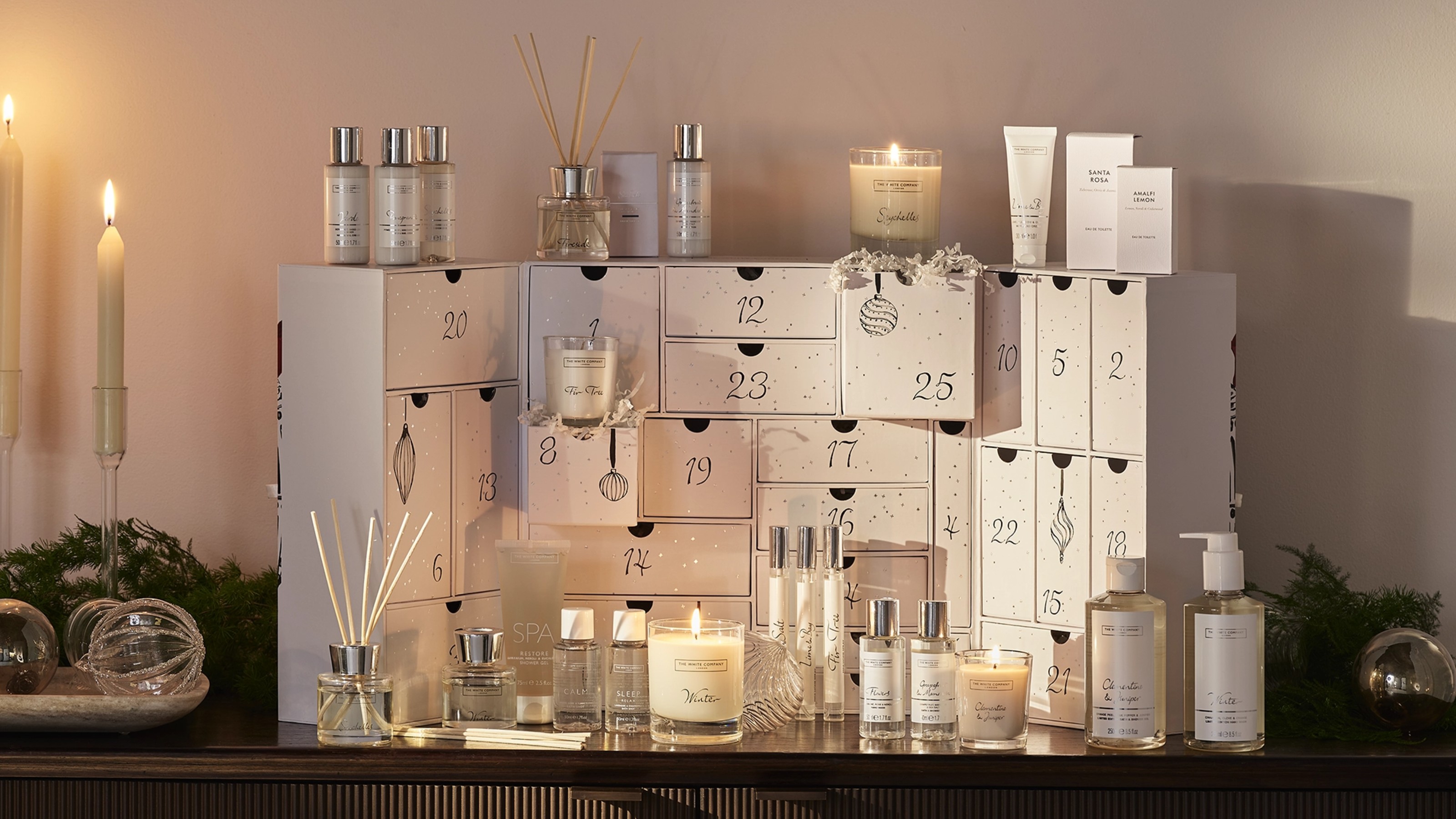 The White Company advent calendar 2025 on a dark wood sideboard next to lit dinner candles
