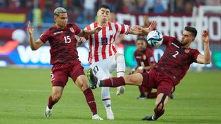 Miguel Almiron (C), in white and red stripes, battles for possession with Miguel Navarro and Wilker Angel, both in red shirts.