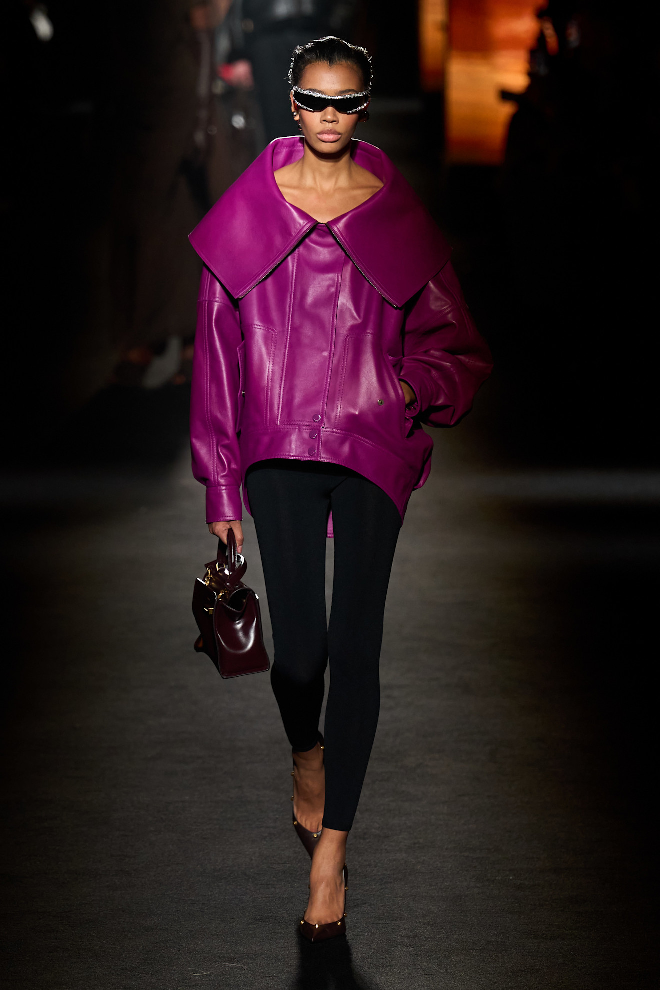 A model walking in the F/W 26 Balenciaga show during Paris Fashion Week wearing a fuchsia leather jacket, leggings, and pumps.