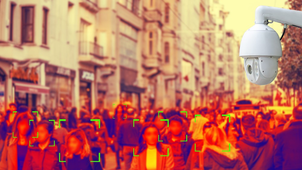 An oversaturated image shows a surveillance camera and a crowd of people whose faces are being analyzed.