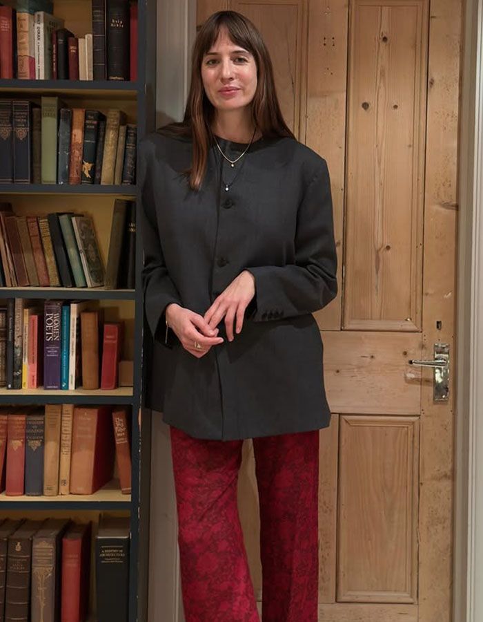 Woman in gray collarless blazer and red pants.