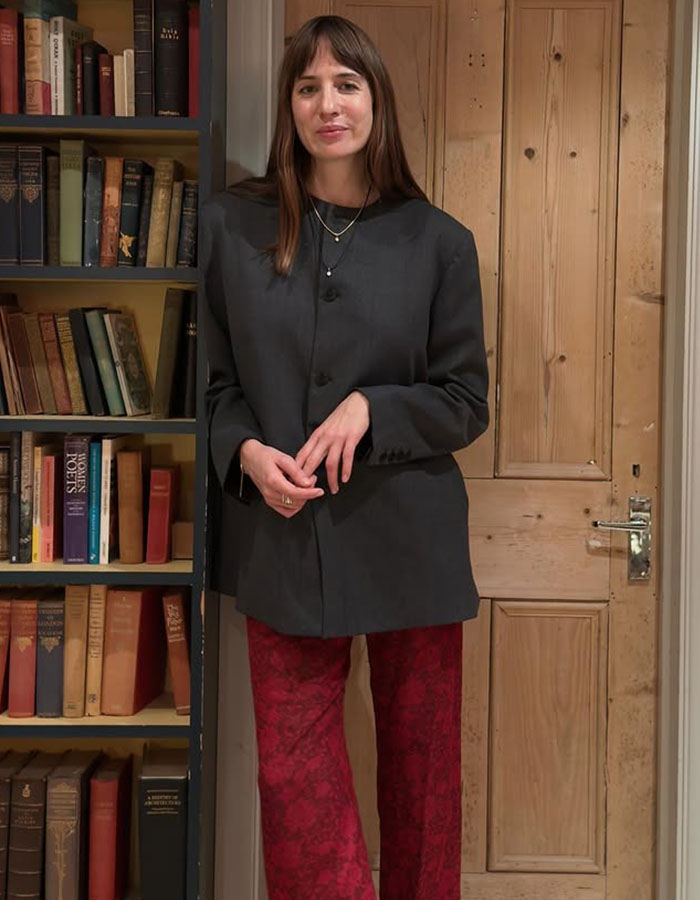 Woman in gray collarless blazer and red pants.